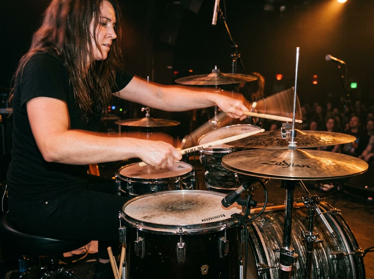 Mains d'un batteur se croisant pour frapper simultanément une cymbale charleston et une caisse claire avec un effet de mouvement dynamique sous les projecteurs.