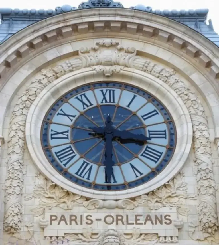 Façade du musée d'Orsay avec son horloge emblématique, la Seine au premier plan par une journée ensoleillée.